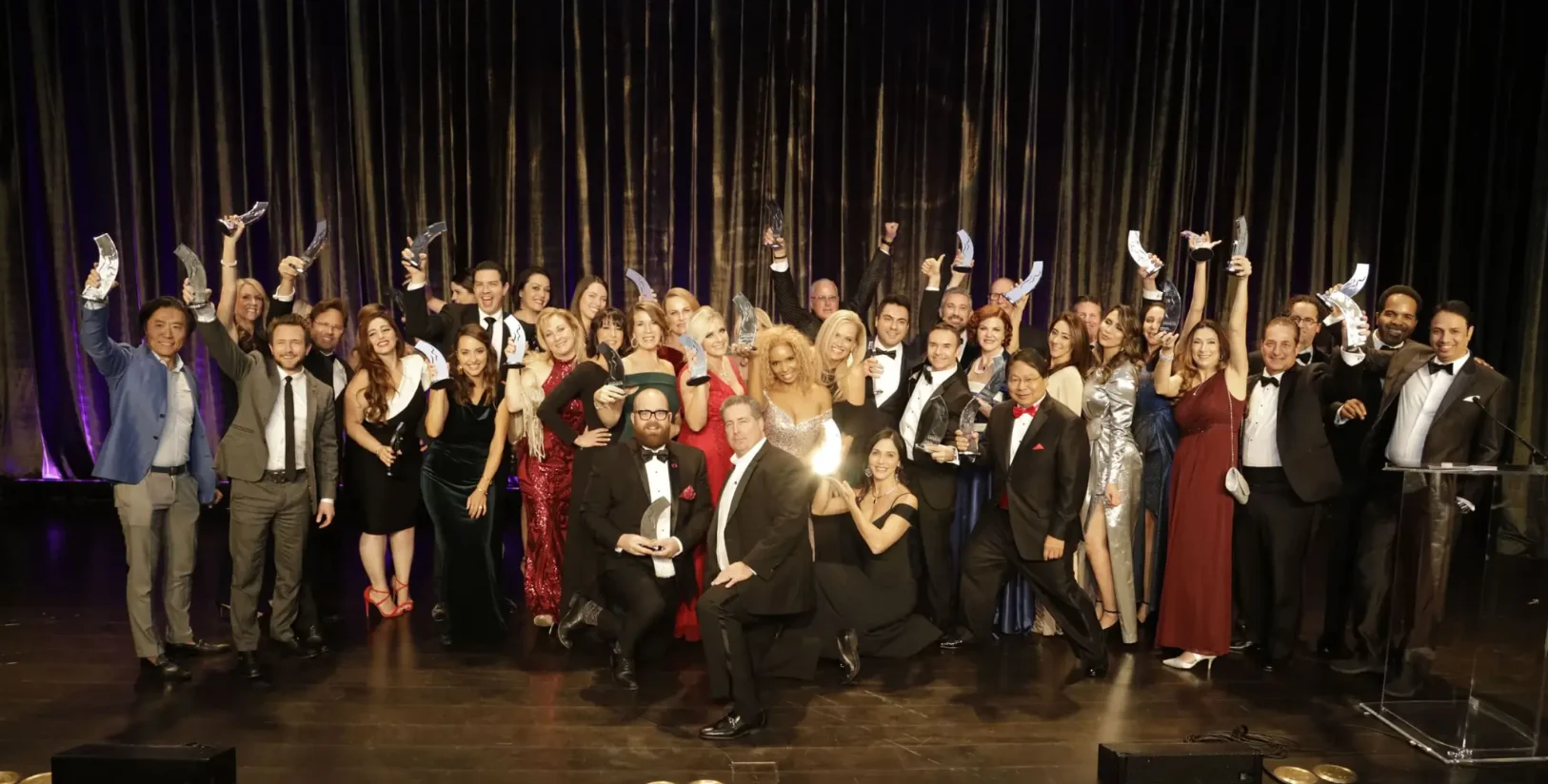 A stage full of MyFaceMyBody Awards winners raising their trophies