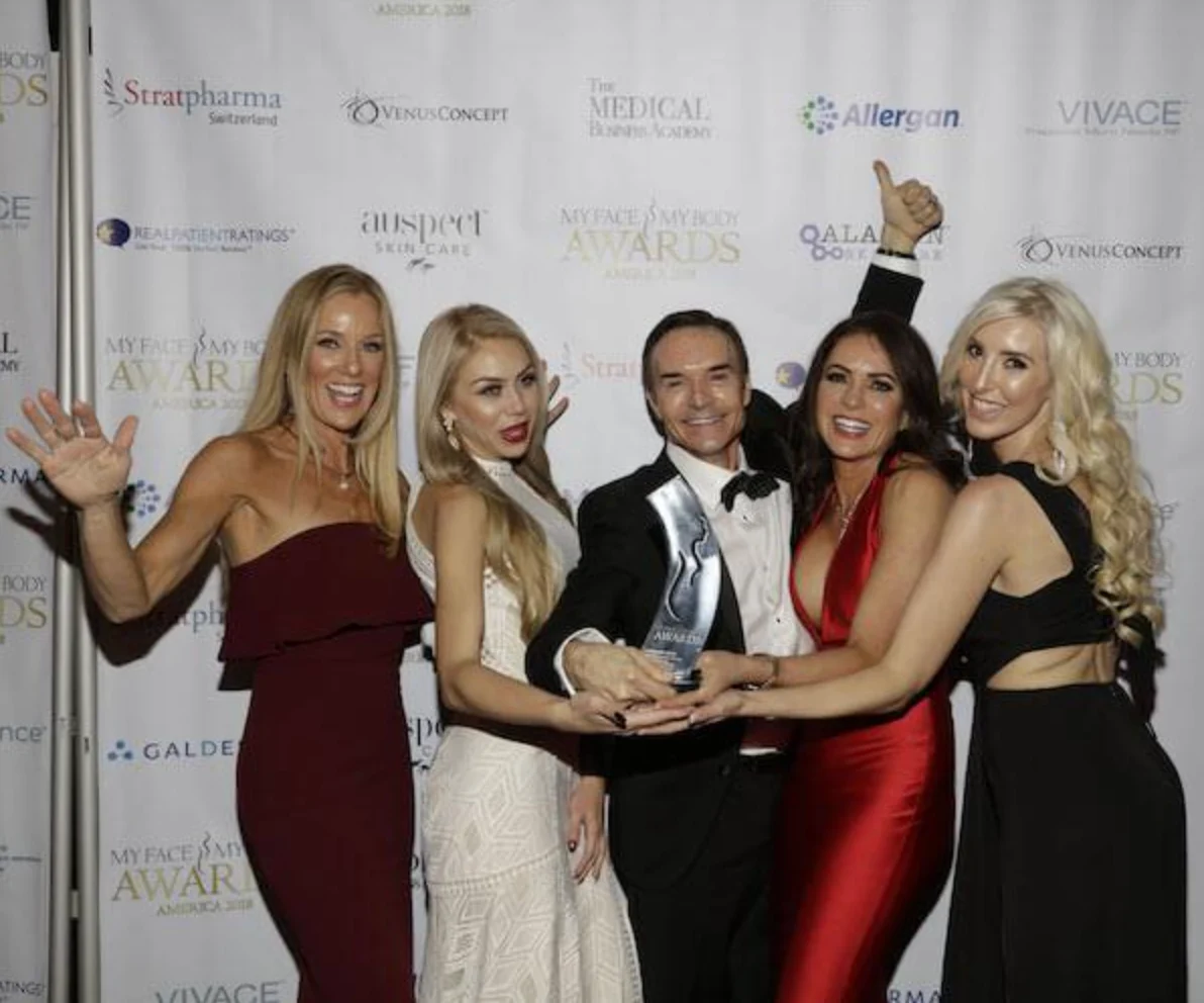 Award winners celebrating with a MyFaceMyBody Awards trophy in front of the awards sponsor backdrop